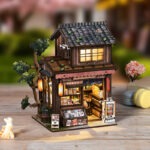 Spring Day Book Nook Miniatur eines japanischen Geschäfts mit warmer LED Beleuchtung, kleinen Regalen, Baumdetails und realistischer DIY Szenenwirkung.