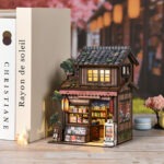 Spring Day Book Nook Miniatur eines japanischen Ladens mit beleuchteter Fassade, Verkaufsregalen, Baumdetails und stilvoller DIY Dekoration.