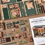 Aura Verde Flower Room Book Nook DIY kit miniature parts layout showing floral decorations, wooden pieces, craft accessories, assembly manual, and detailed components for building the miniature room.