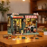 Aura Verde Flower Room Book Nook miniature flower shop display with warm LED lighting, colorful floral decorations, striped awning, wooden furniture, and DIY assembly pieces on the table.