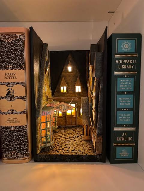 Beleuchtetes Book Nook mit schmaler magischer Gasse, alten Hausfassaden und warmen Laternen zwischen Fantasybüchern